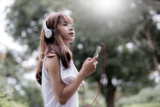 Young beautiful woman standing  and listen to music after jogging during sunlight