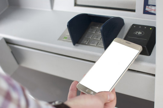 Hand of a man with a credit card, using an ATM. Man using an atm machine with his credit card. Closeup of male hands using smart phone while typing on ATM.
