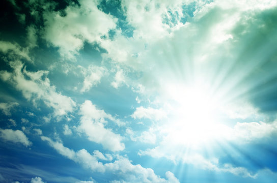 Blue sky with white and gray cumulus clouds. Bright sun with blue rays