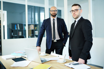 Serious businessman and his co-worker looking at camera