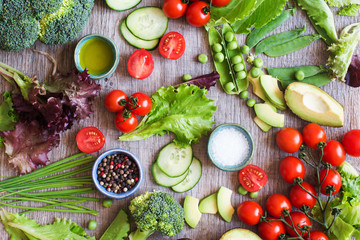 Cut ingredients for salad, fresh tomatoes, cucumber, avocado, lettuce, spring onion, broccoli on the grey wooden table, top view selective focus