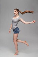 Beautiful barefooted full length female in denim shorts and grey tshirt jumping over grey...
