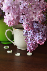 Porcelain teacup, lilac bouquet and white decors on brown table