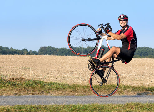 Cheerful cyclist riding on the rear wheel. Biker balancing while driving on a road bike. Risky ride on one wheel.