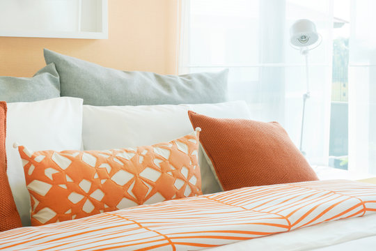 Orange, white and gray pillows on bed in modern bedroom interior