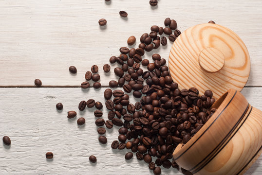 Coffee beans scattered from a Cup on white wooden background, wooden utensils,