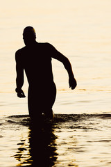 Silhouette of a triathlete enters the water.