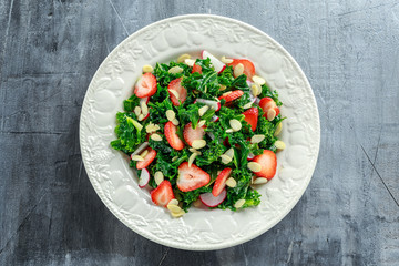 Healthy kale salad with strawberries and almond in a white plate