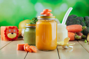 Jars with vegetable and fruit puree and juice near fresh vegetables, toys and dummy