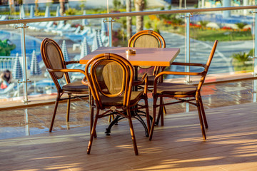 Tables and chairs in the cafe on the terrace. There are no visitors. In the background, you can see the pool. On standing ashtrays for smokers.