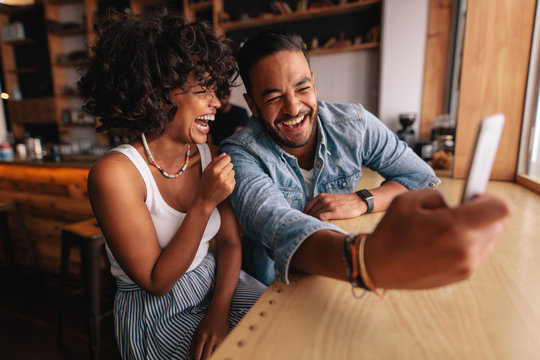 Laughing couple taking selfie at coffee shop