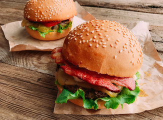 Bright juicy appetizing burgers with a cutlet, cheese, marinated cucumbers, tomatoes and bacon in the hands of a girl, a girl in special gloves for burgers