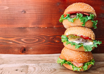 Bright juicy appetizing burgers with a cutlet, cheese, marinated cucumbers, tomatoes and bacon in the hands of a girl, a girl in special gloves for burgers