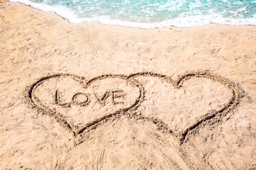 Word LOVE and hearts drawn on sand near water. Romantic concept