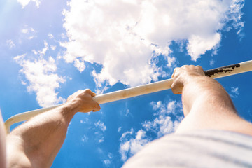 First-person view of the horizontal bar. The guy pulls up on the bar. Workout outdoors. Blue sky on...