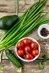 Fresh vegetables on a wooden background- avocado, cherry tomatoes, cucumber, spring onions and spices.Food background.Top view