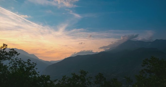 Snowcapped mountain ridges and peaks with moving clouds over the Alps in summer, Torino Province, Italy. Time lapse fading from sunlight to dusk.
