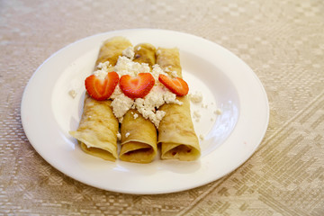 Dessert made from pancakes stuffed with cottage cheese and strawberries. Is on a table in a white plate