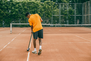 A young man in a sports uniform is cleaning a tennis court. The tennis player is preparing a court for the game.