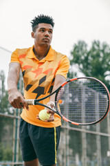 Low angle view of determined young black man playing tennis. Tennis player posing in front of a tennis court