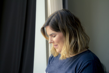 Cute lovely shy smiling young woman standing near the window