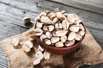 Pistachios in wooden bowl over wooden background, selective focus.