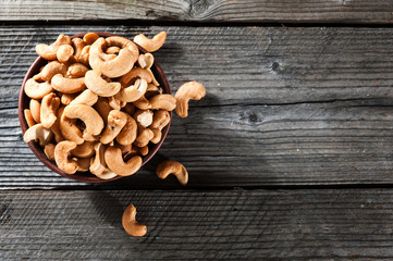 Raw cashew nuts in bowl on textured wooden background, table top view, selective focus