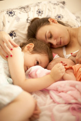Happy Mother Laying in Bed with Daughter and Newborn Baby