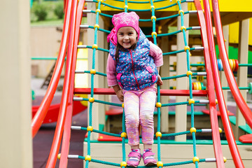 Fototapeta na wymiar Portrait of Happy little blond girl playing on a rope web playground outdoor