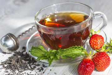 tea time/cup of tea, tea leaves,tea maker, mint leaves and strawberries on light wooden table