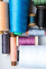 tailoring, sewing, patchwork and concept - closeup on blue, white, black, apricot, pink, purple and green color threads in new bobbins on white background at workshop, top view, flat lay