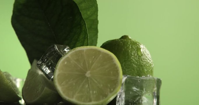 lime turning on it's axis on green background covered by water drops with ice cubes
