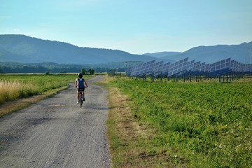 Ecological energy. Solar power plant and cycle path. A cycling cyclist rides along a cycle path next to the background Nature, forests and mountains. Slovakia, Europe.