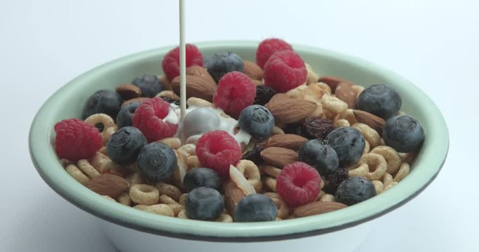 milk pouring to the bowl with corn flakes rings with berries and nuts.