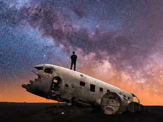 Silhouette of Man Standing on Crashed Airplane Gazes Deeply Into the Milky Way Galaxy on a Clear...