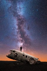 Silhouette of Man Standing on Crashed Airplane Gazes Deeply Into the Milky Way Galaxy on a Clear Starry Night Sky - Vertical