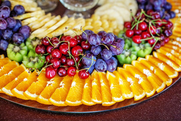 A fruit dish with oranges, kiwi fruit, grapes, cherries and pineapples. The concept of healthy food and vegetarian.