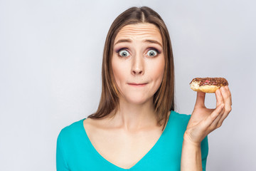 Portrait of beautiful girl with chocolate donuts. amazed and looking at camera with surprised big eyes. studio shot on light gray background.