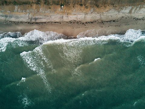 Aerial photo of coastline on a stormy day hitting a beach cliff overlooked by a forest