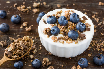 Serving of Yogurt with Whole Fresh Blueberries and Muesli on Old Rustic Wooden Table. Closeup Detail.