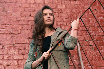 stylish girl in military style, black dress near red brick wall, film photo