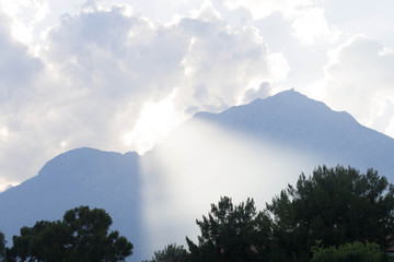 Picturesque view to the mountain partly lighted with wide light ray from the clouds