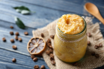 Glass jar with scrub, dried lemon slice and coffee grains on wooden background