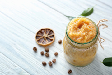 Glass jar with scrub, coffee grains and dried lemon slice on wooden table