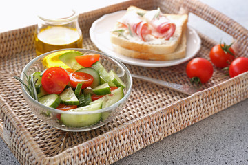 Tasty salad and sandwich for breakfast on wicker tray