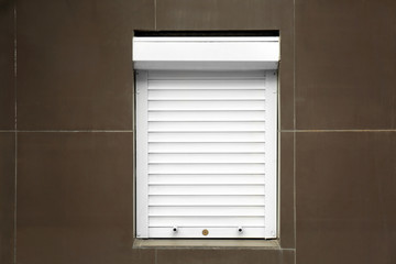 White window with closed roller blind in wall
