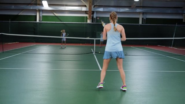 A young athlete beats off tennis balls during training with her partners, a woman in a sport suit actively runs around the tennis court