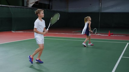 An adult boy and his girlfriend in a sports suit and sneakers beat off tennis balls during a sports training in a closed sports complex