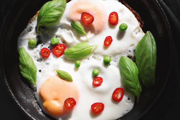 Delicious over hard eggs with green peas, pepper and basil leaves in pan, closeup