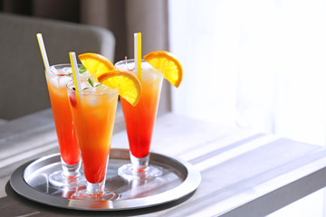 Glasses of Tequila Sunrise cocktail on metallic tray